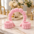 Pink plush spa headband with two matching wristbands on an ivory vanity